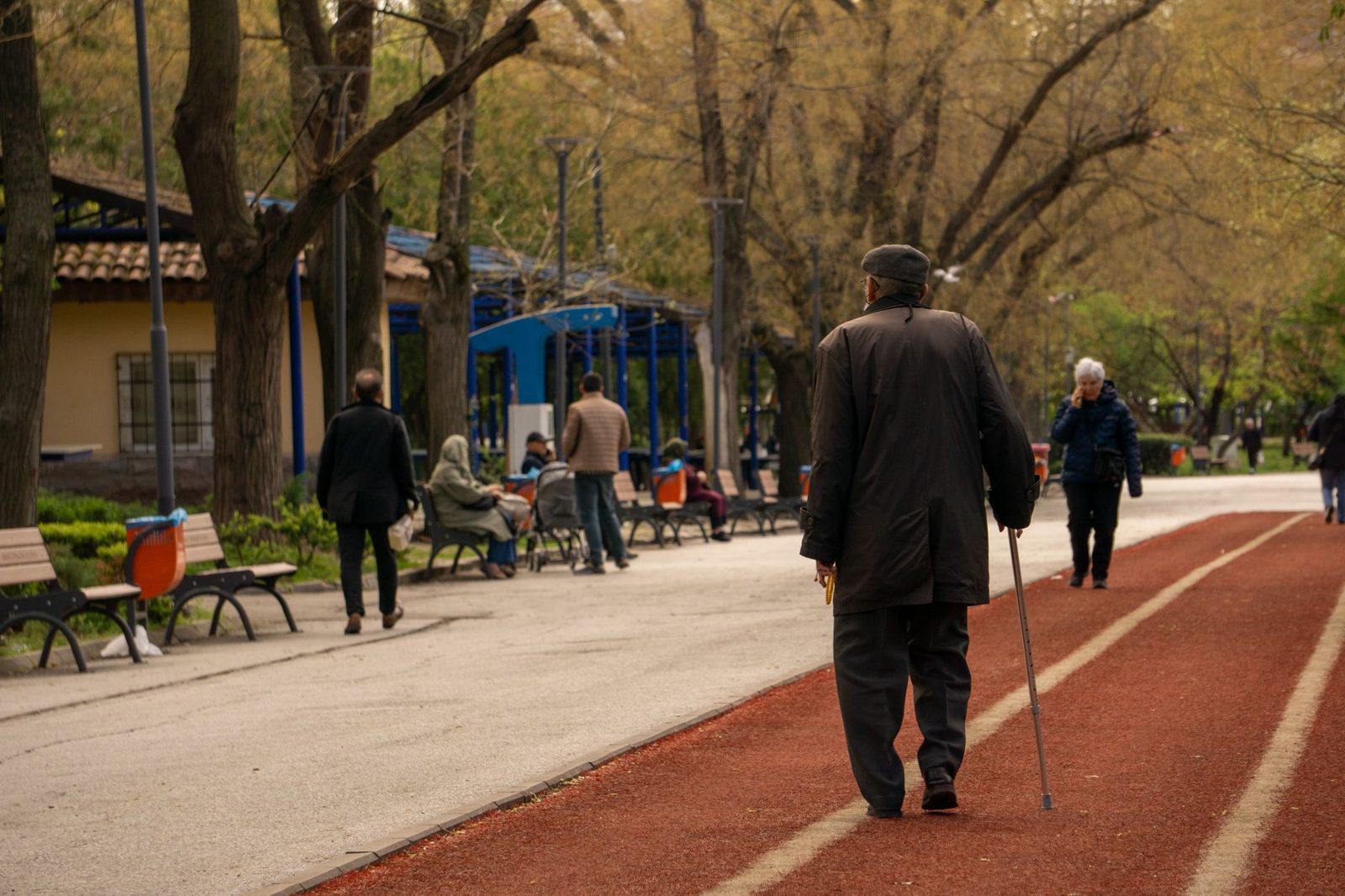 Older man walking with a cane along a park path