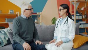 Doctor talking with an older man on a sofa during a home visit