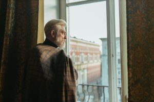 Older man standing at a window, looking out