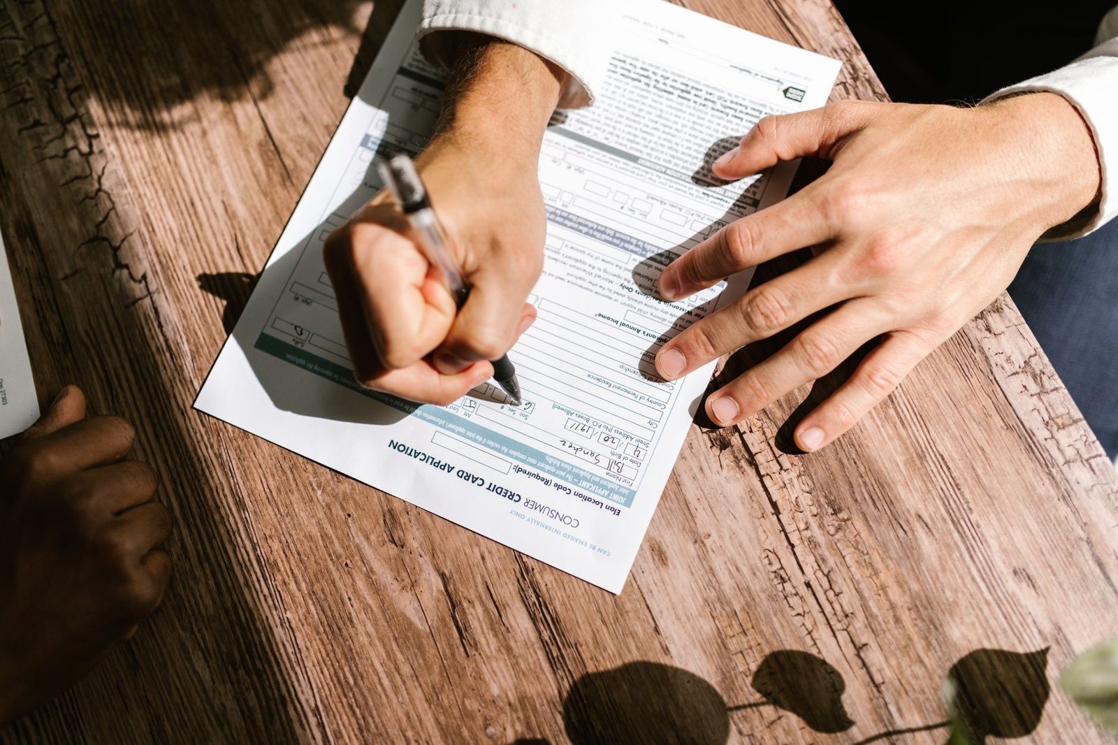 Hands filling out an application form on a wooden table