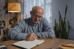 Older man writing in a notebook at a table