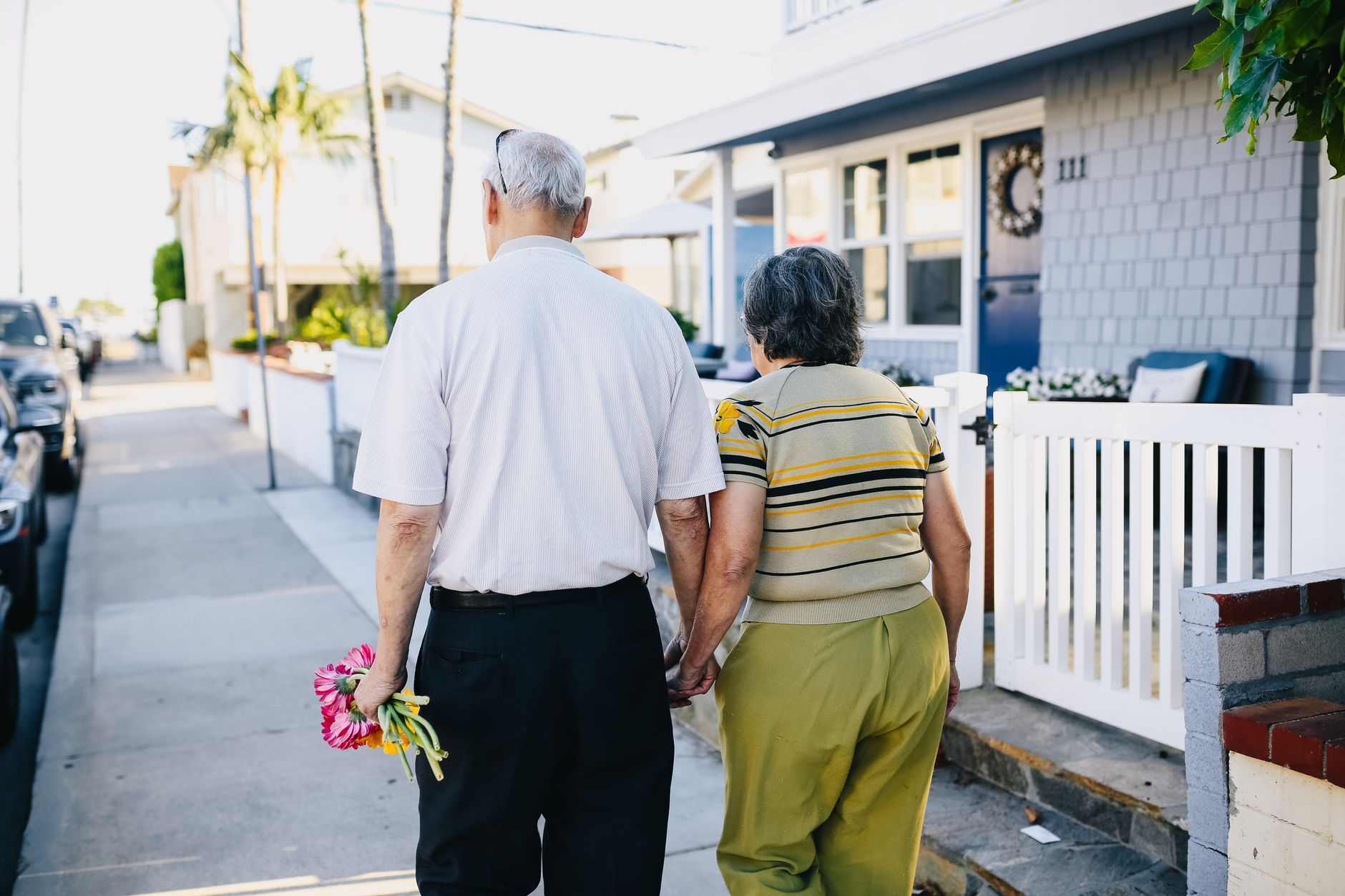 An older couple walking hand in hand along a sunny sidewalk
